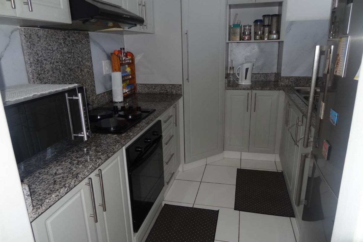 A compact, well-maintained kitchen featuring grey cabinetry, granite countertops, built-in oven, electric hob, and tiled flooring.