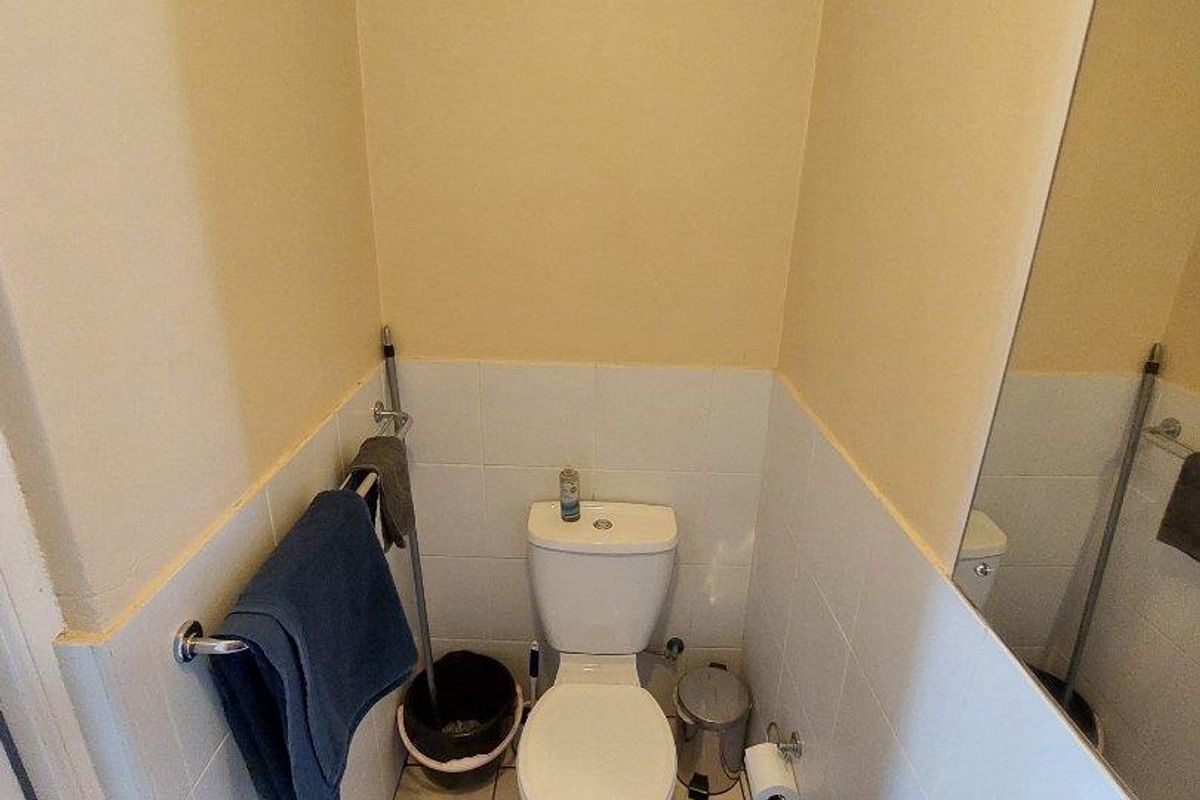 A compact guest bathroom featuring a white pedestal basin, a standard toilet, and a large wall-mounted mirror with tiled splashbacks.
