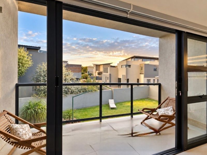 A modern covered balcony featuring tiled flooring and a sleek glass balustrade, offering a pleasant view of the surrounding residential area.