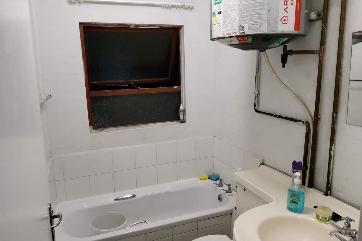 A functional bathroom featuring a built-in bathtub, vanity basin, and wall-mounted electric water heater, requiring cosmetic updates to modernize the space.
