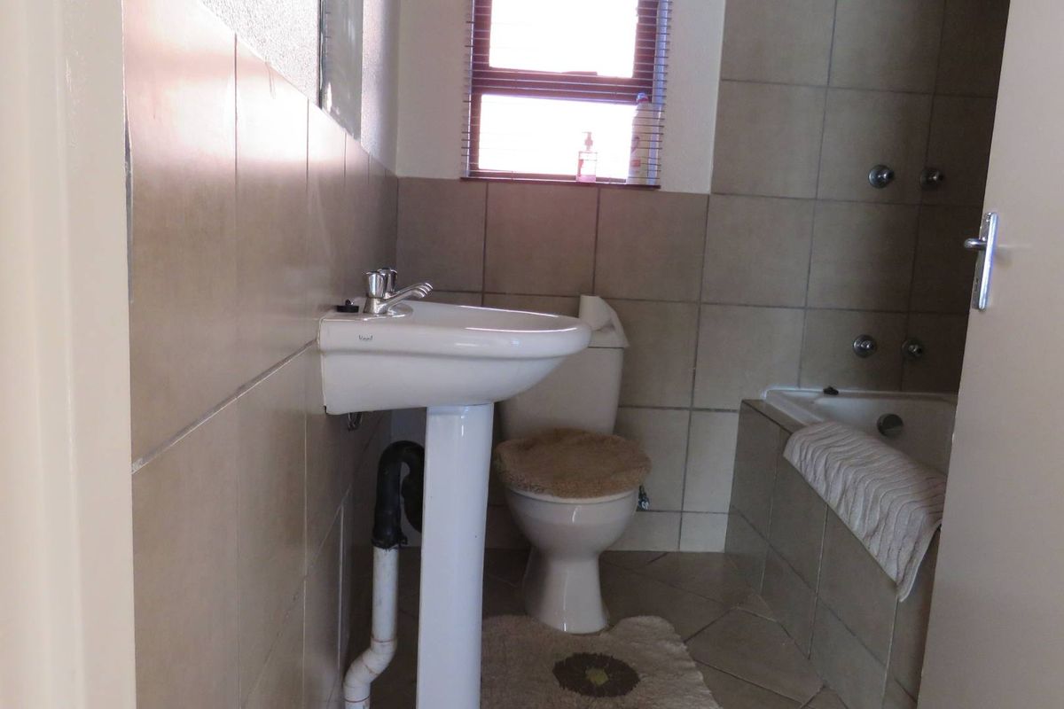 A functional bathroom featuring a pedestal basin, a standard toilet, and a tiled bathtub with wall-mounted fixtures.