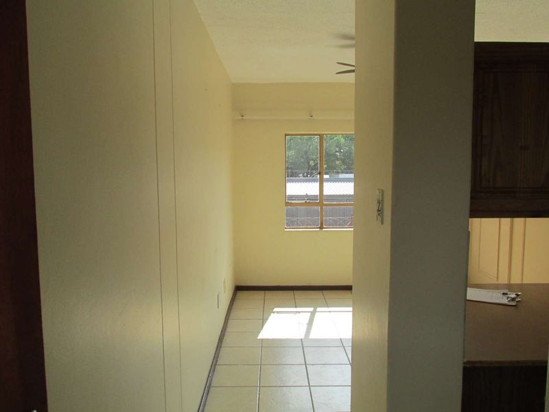 A view through a hallway with tiled flooring leading towards a window, showing a neutral interior space.