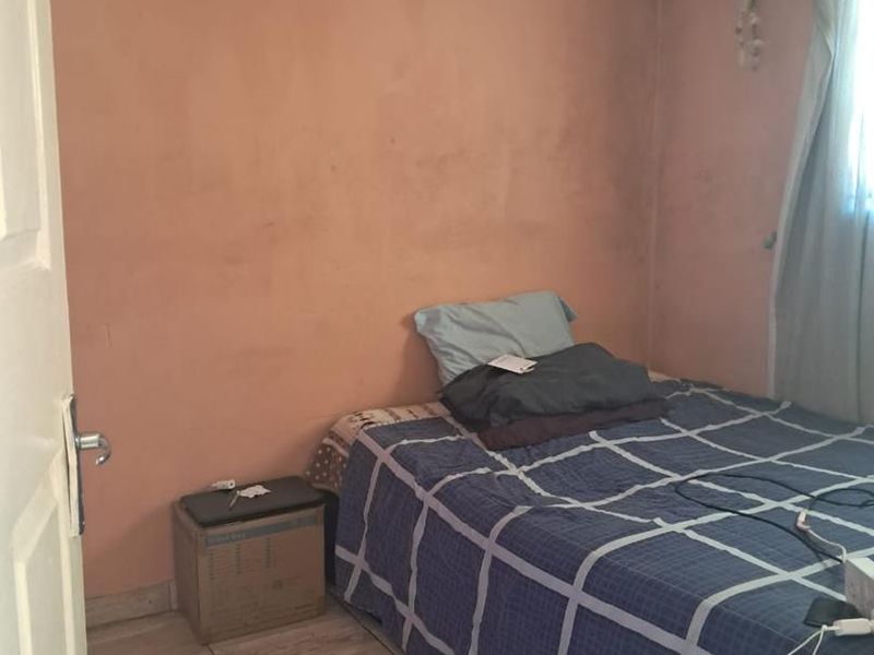 A compact bedroom featuring tiled flooring and a textured ceiling, currently requiring cosmetic updates to the wall finishes and ceiling maintenance.