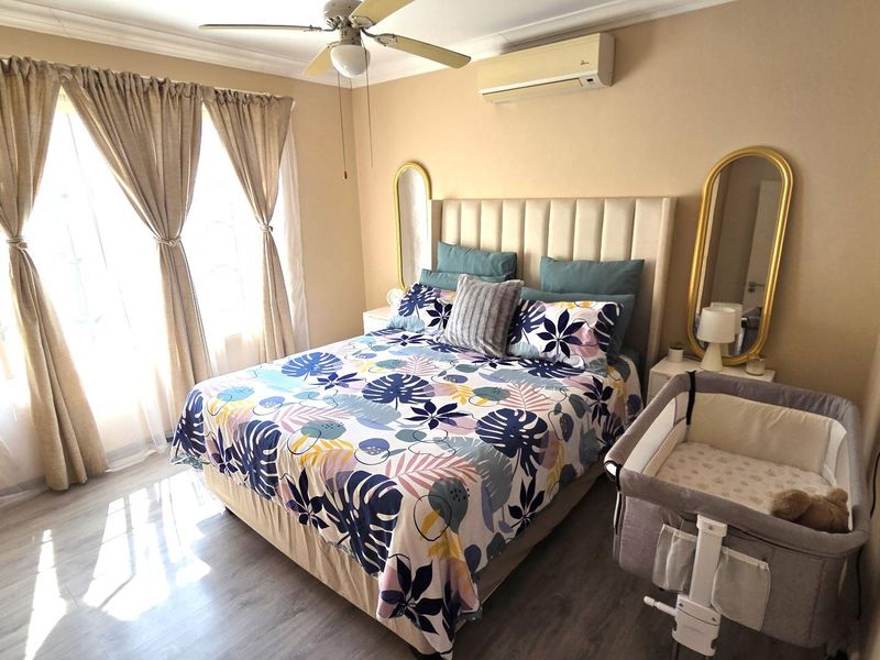 A well-maintained bedroom featuring laminate flooring, a ceiling fan, and a wall-mounted split-system air conditioner for climate control.