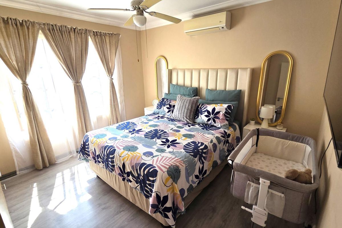 A well-maintained bedroom featuring laminate flooring, a ceiling fan, and a wall-mounted split-system air conditioner for climate control.