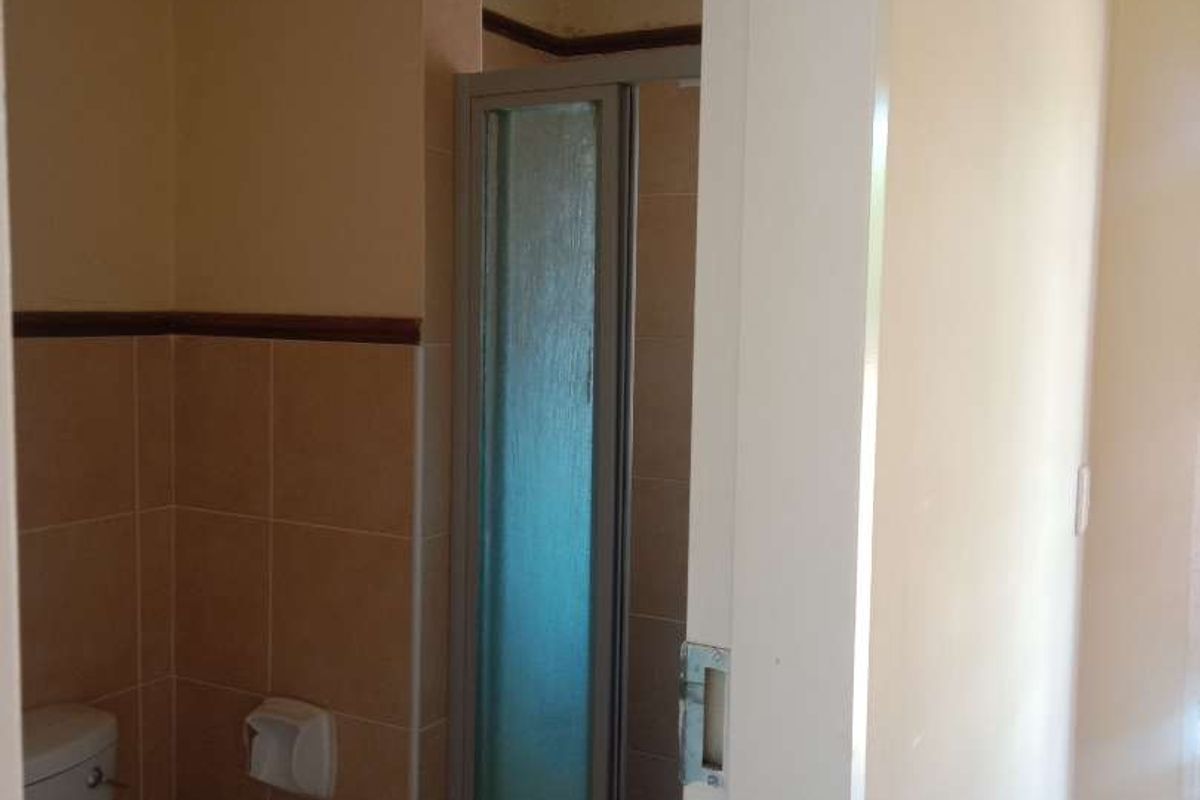 A compact bathroom featuring a shower enclosure and toilet, currently showing signs of ceiling water damage and requiring maintenance.