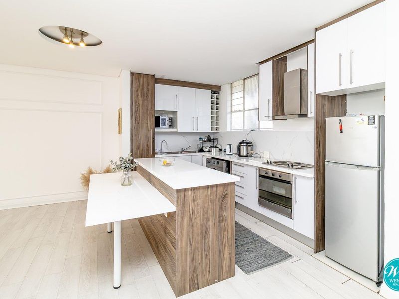 Modern kitchen featuring white and wood-grain cabinetry, stone countertops, a central island with an integrated breakfast bar, and stainless steel appliances.