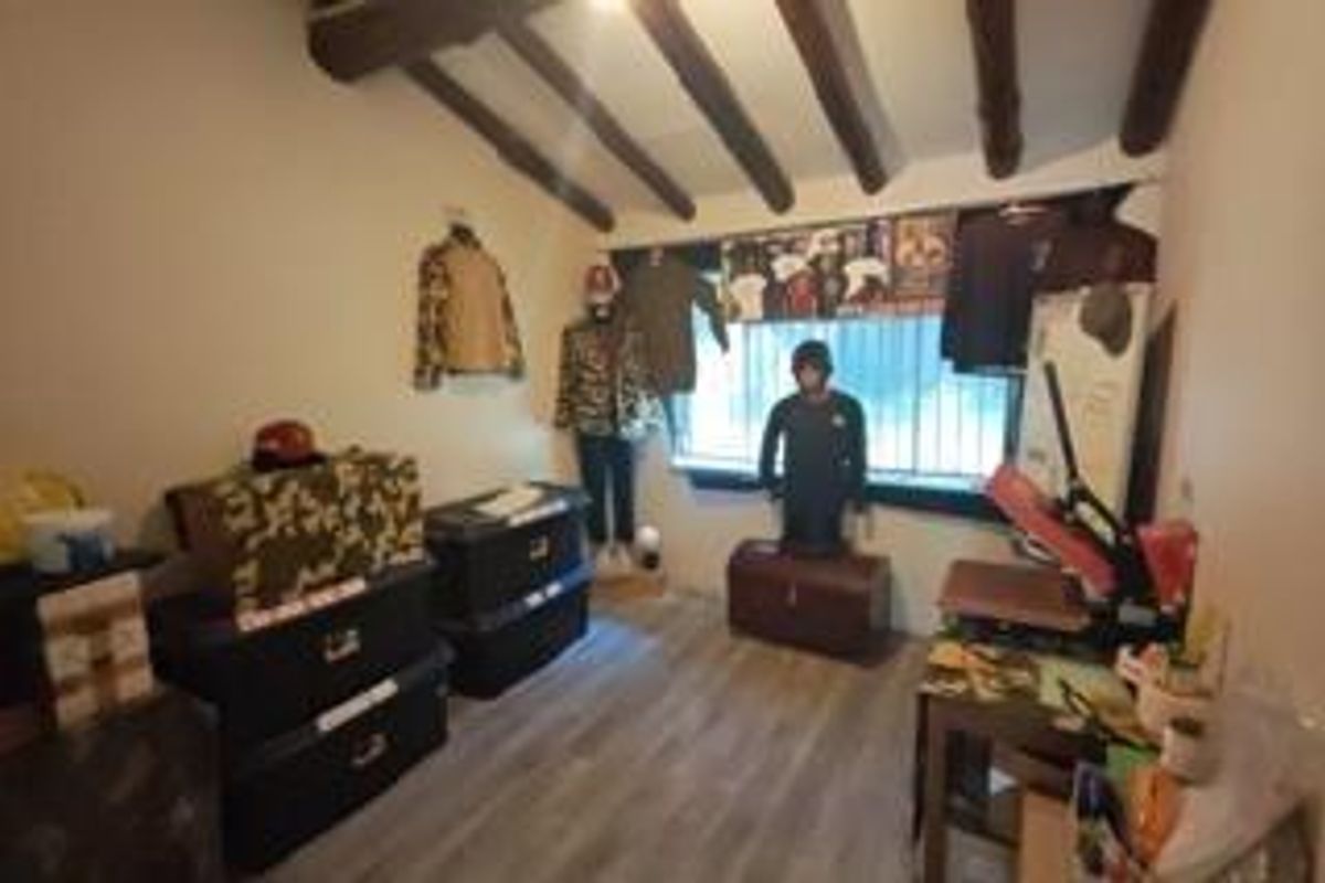 A bedroom featuring exposed timber ceiling beams, laminate flooring, and a window fitted with security bars.