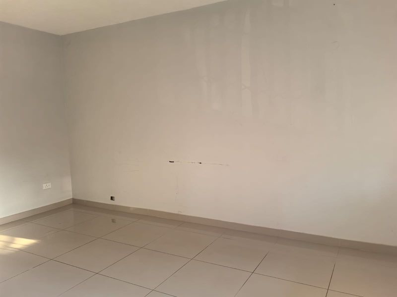 An empty living area featuring neutral tiled flooring and plain walls with visible surface imperfections requiring minor repair.
