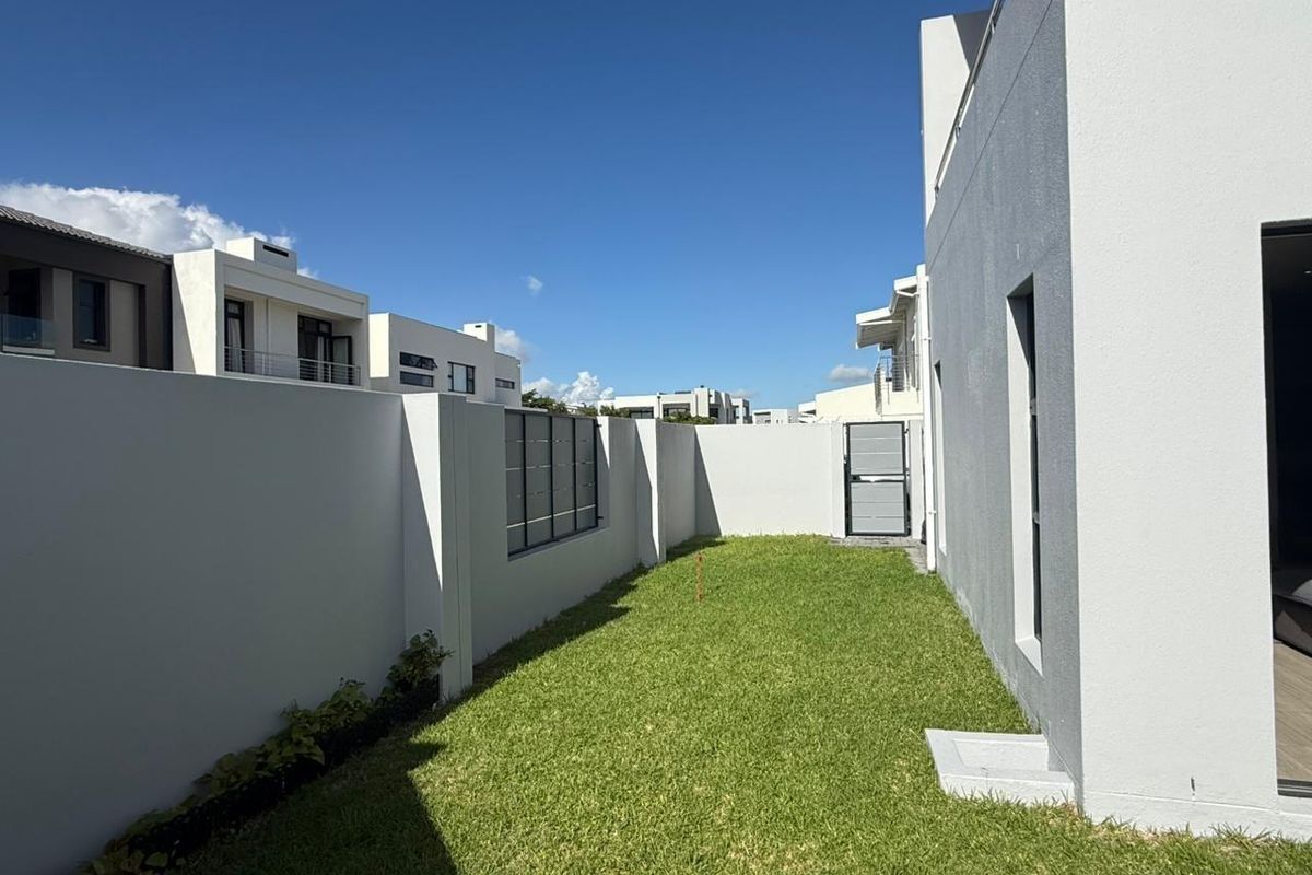 A well-maintained rear garden area featuring a manicured lawn, perimeter boundary walls, and a secure metal gate.