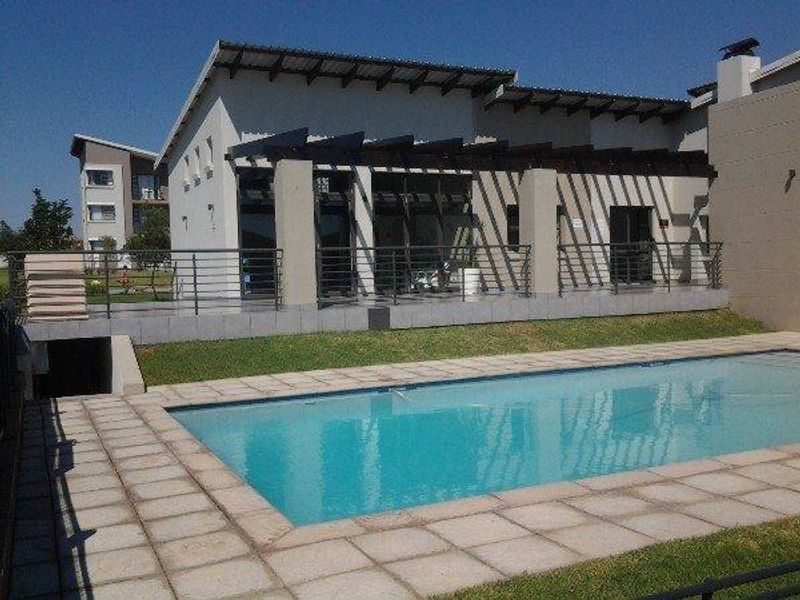 Exterior view of a swimming pool area featuring a paved surround, a covered patio with a timber pergola, and modern sliding glass doors.