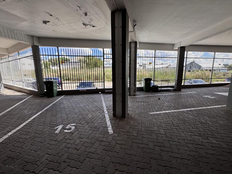 Covered parking area featuring paved bays, steel security fencing, and concrete structural elements with visible ceiling wear.