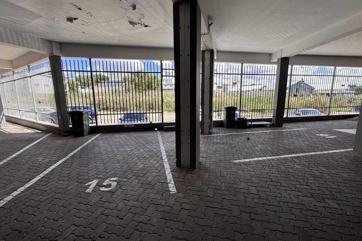 Covered parking area featuring paved bays, steel security fencing, and concrete structural elements with visible ceiling wear.