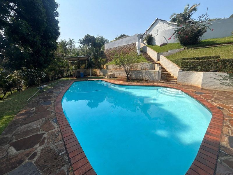 Outdoor pool area featuring a swimming pool with brick coping, stone paving, and tiered retaining walls with concrete stairs leading to the upper garden level.