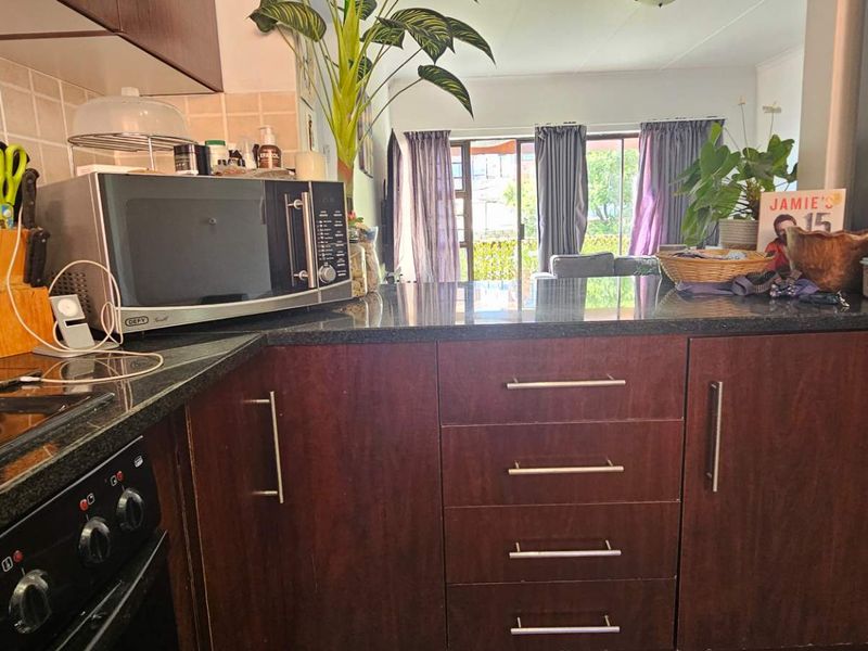 Open-plan kitchen featuring dark wood cabinetry, granite countertops, and a tiled backsplash, flowing into a living area with access to the patio.