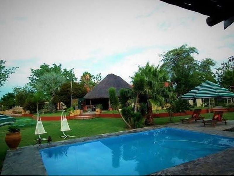 Outdoor pool area featuring a swimming pool, stone paving, and a view of a traditional thatched roof structure set within a landscaped garden.