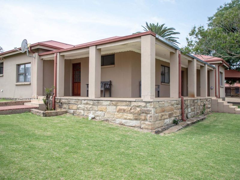 Rear view of the farmhouse featuring a covered patio with stone cladding, metal roofing, and surrounding lawn area.
