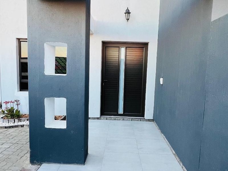 A modern front entrance featuring a tiled porch, dark contemporary front door, and architectural pillar detailing with integrated lighting.
