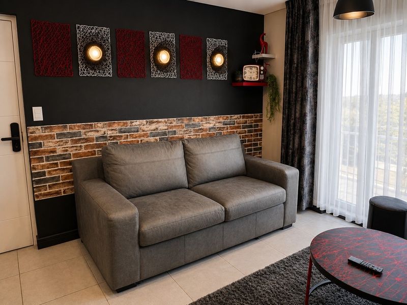 A modern living room featuring a striking black accent wall with brick veneer detailing, tiled flooring, and direct access to a balcony through sliding doors.