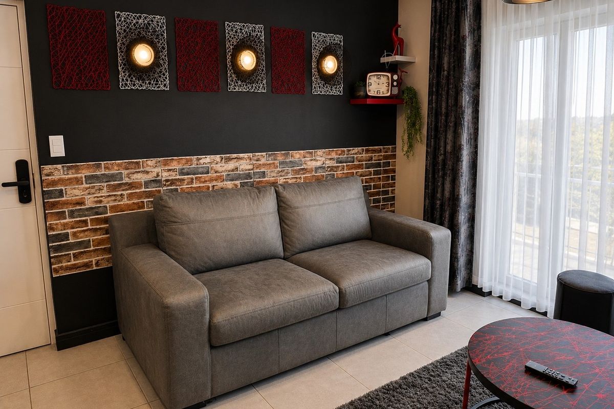 A modern living room featuring a striking black accent wall with brick veneer detailing, tiled flooring, and direct access to a balcony through sliding doors.