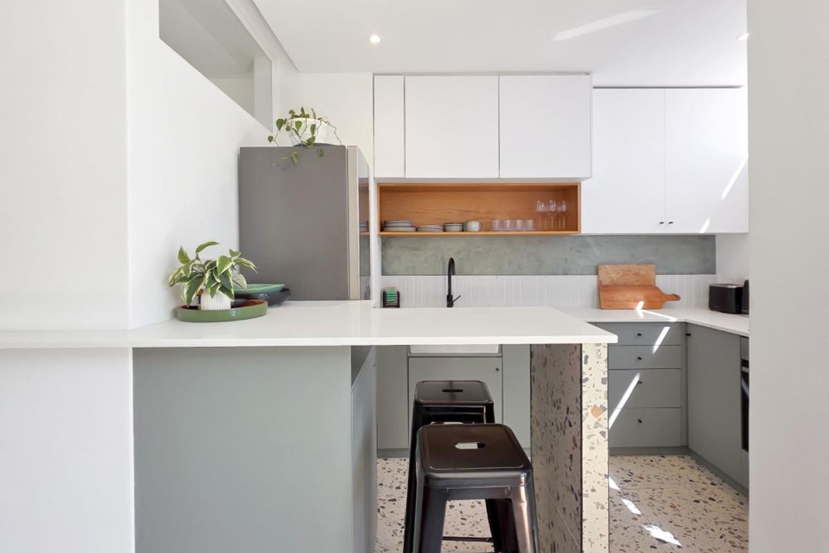 Modern kitchen featuring sleek white and grey cabinetry, terrazzo flooring, a stone breakfast bar, and a stylish tiled backsplash with integrated sink.