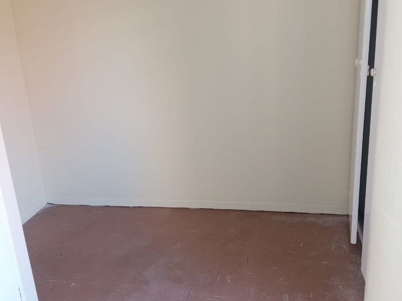 An empty bedroom featuring plain walls and worn floor tiles, offering a blank canvas for renovation or interior design updates.