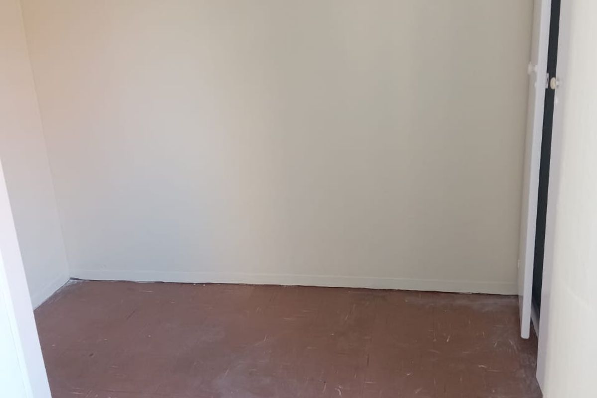 An empty bedroom featuring plain walls and worn floor tiles, offering a blank canvas for renovation or interior design updates.