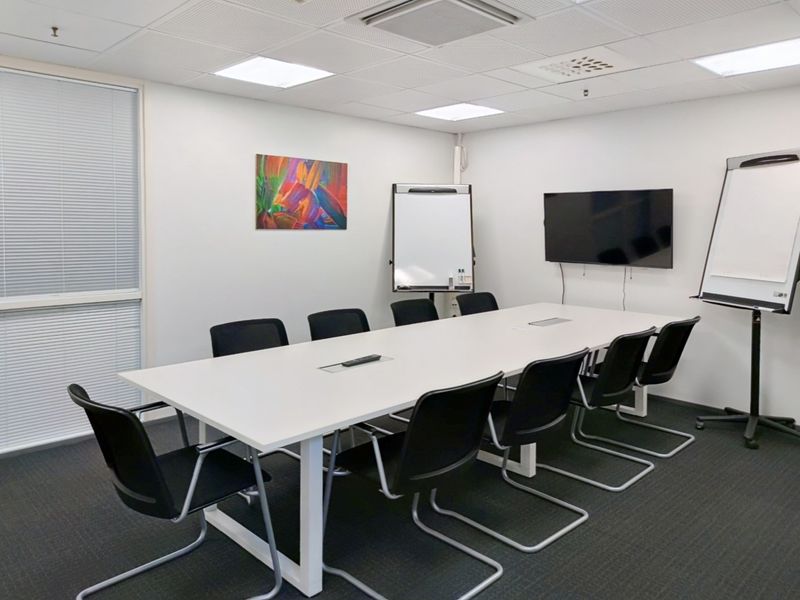 A professional office meeting room featuring a large conference table, suspended ceiling with recessed lighting, and carpeted flooring.