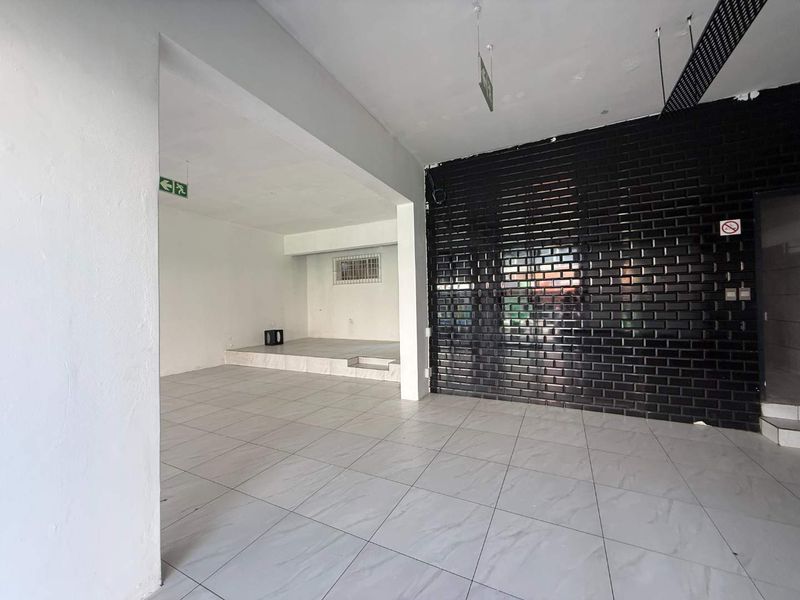 An open-plan retail space featuring light-colored tiled flooring, a raised platform area, and a prominent black security roller shutter.