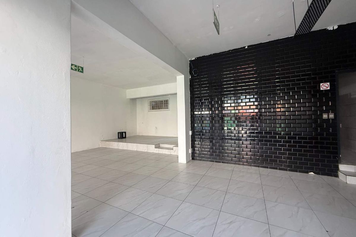 An open-plan retail space featuring light-colored tiled flooring, a raised platform area, and a prominent black security roller shutter.