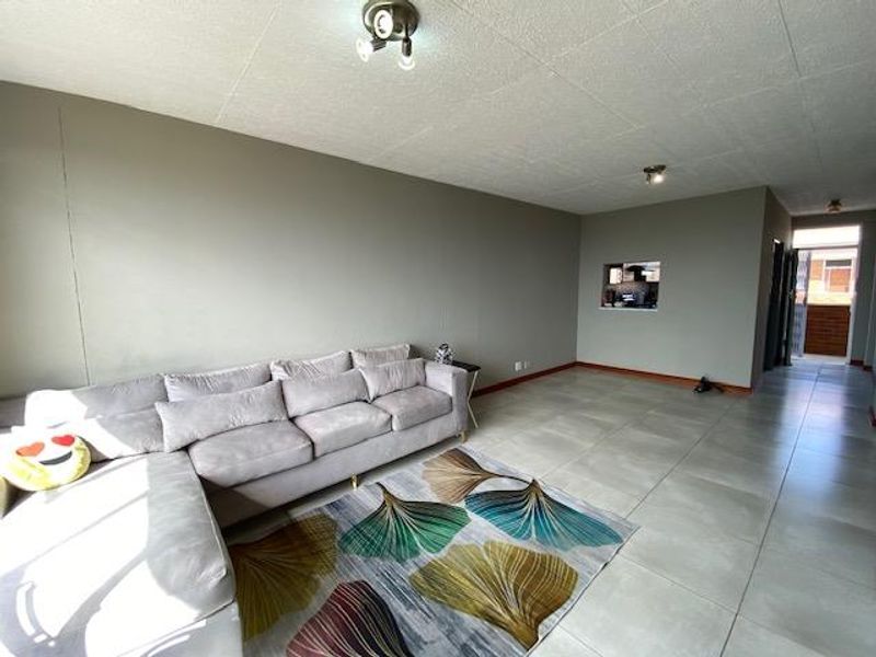 Spacious living area featuring large format floor tiles, neutral wall tones, and a convenient pass-through window connecting to the kitchen space.