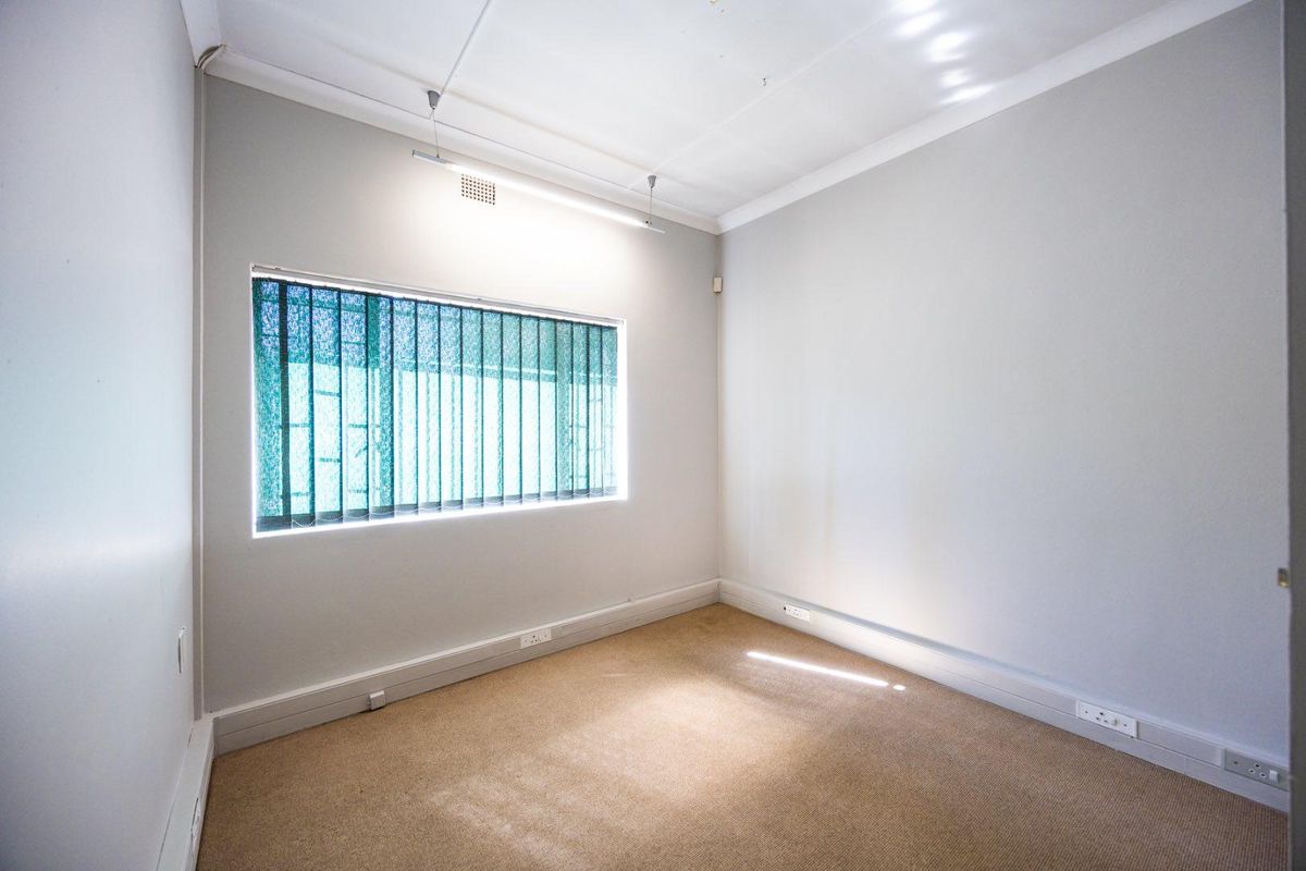 A clean, empty bedroom featuring neutral wall paint, carpet flooring, and a window fitted with vertical blinds.