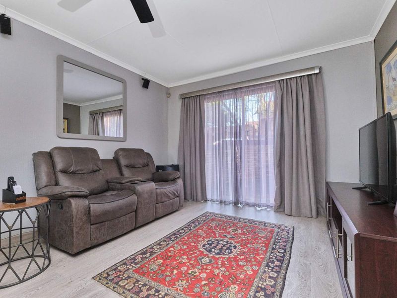 A well-maintained living room featuring light laminate flooring, a ceiling fan, and a sliding glass door providing access to the exterior.