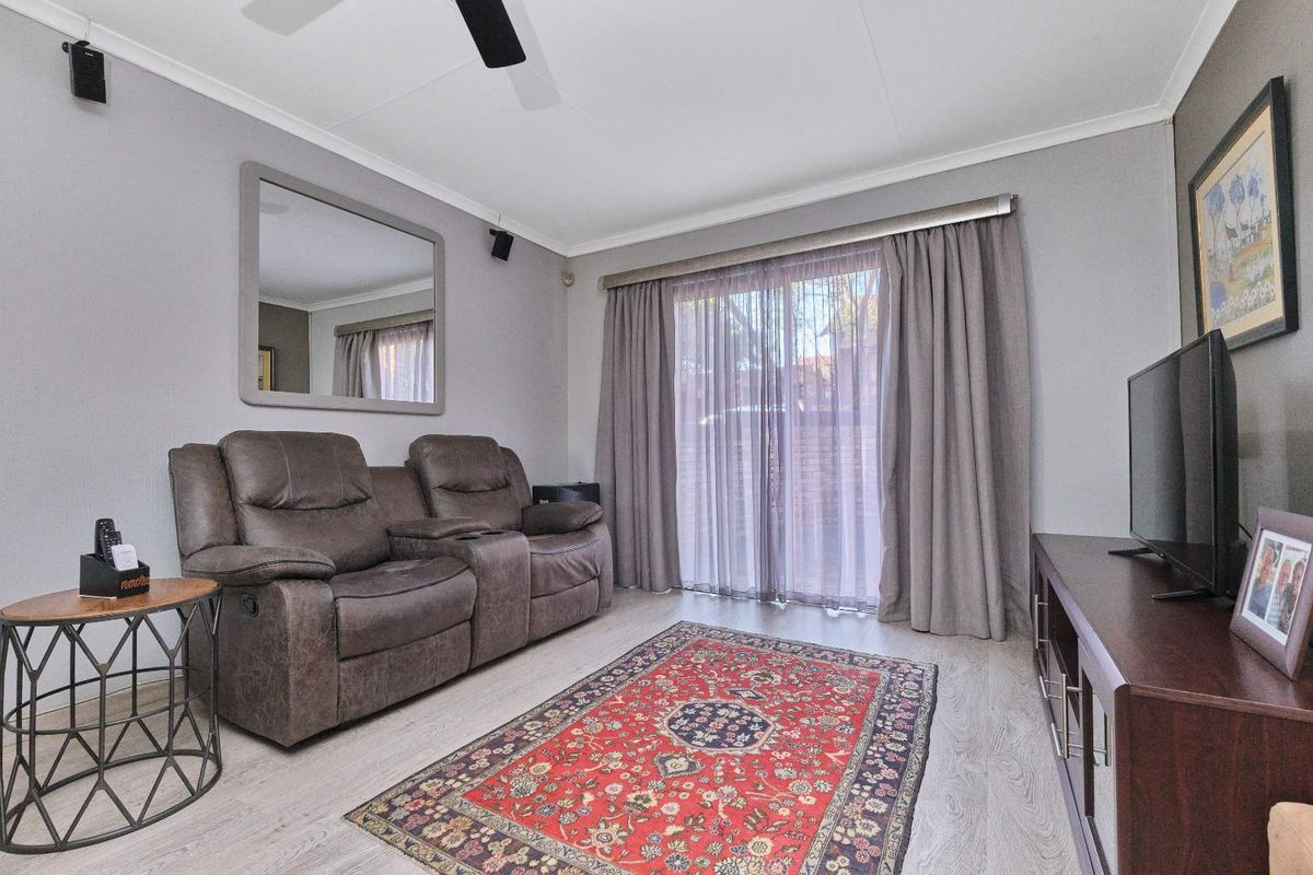 A well-maintained living room featuring light laminate flooring, a ceiling fan, and a sliding glass door providing access to the exterior.