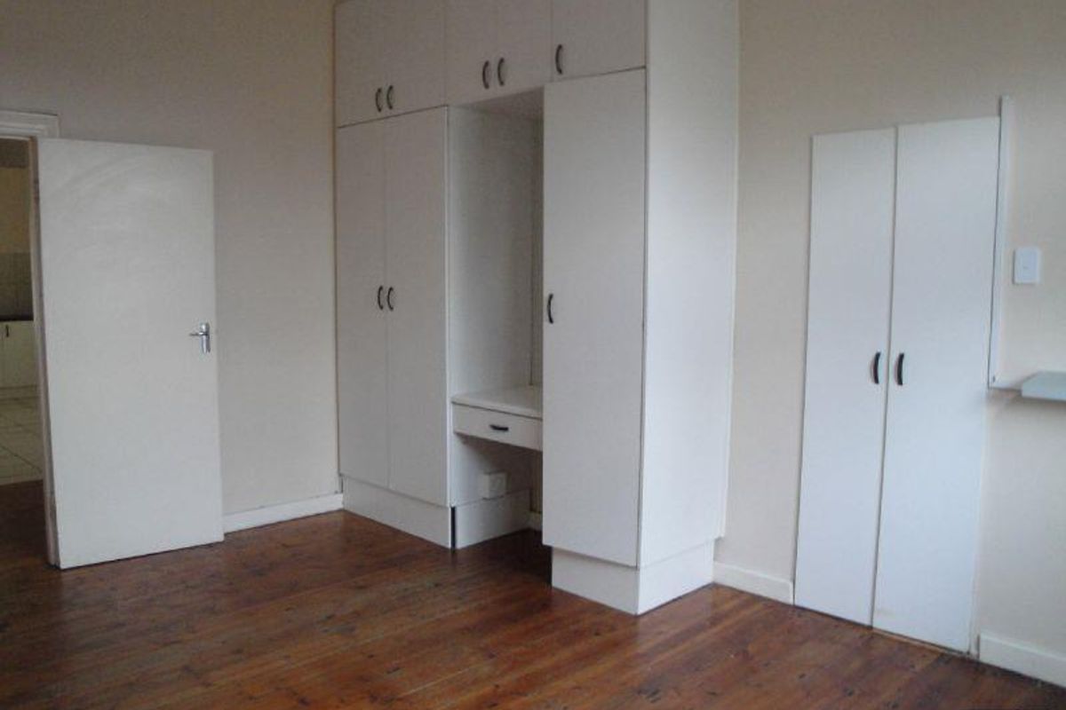 A spacious bedroom featuring polished hardwood flooring and extensive built-in cabinetry with an integrated vanity unit.