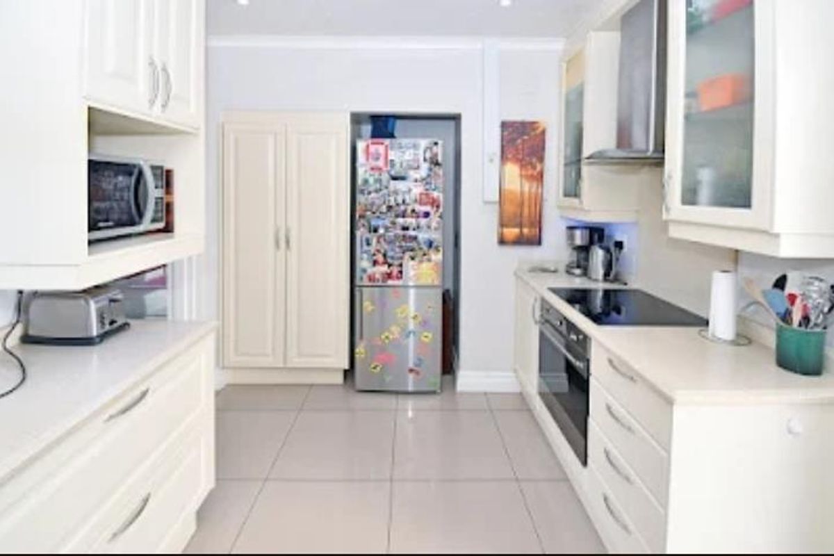 A functional kitchen featuring cream cabinetry, tiled flooring, a built-in oven, electric hob, and an integrated extractor fan.