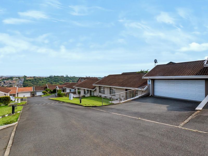 A view of the townhouse complex street, featuring asphalt driveways, tiled roofs, and well-maintained landscaped verges in a residential estate setting.