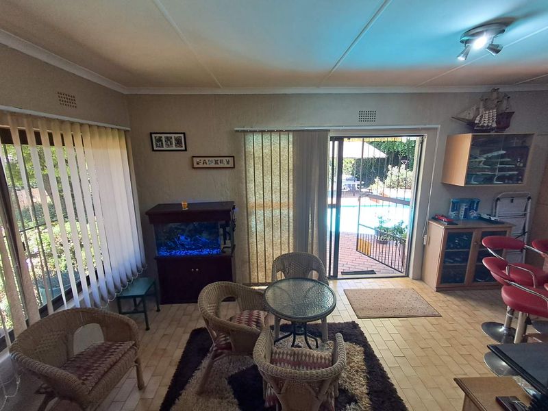 Living area featuring tiled flooring, vertical blinds, and a sliding glass door providing direct access to the outdoor pool area.