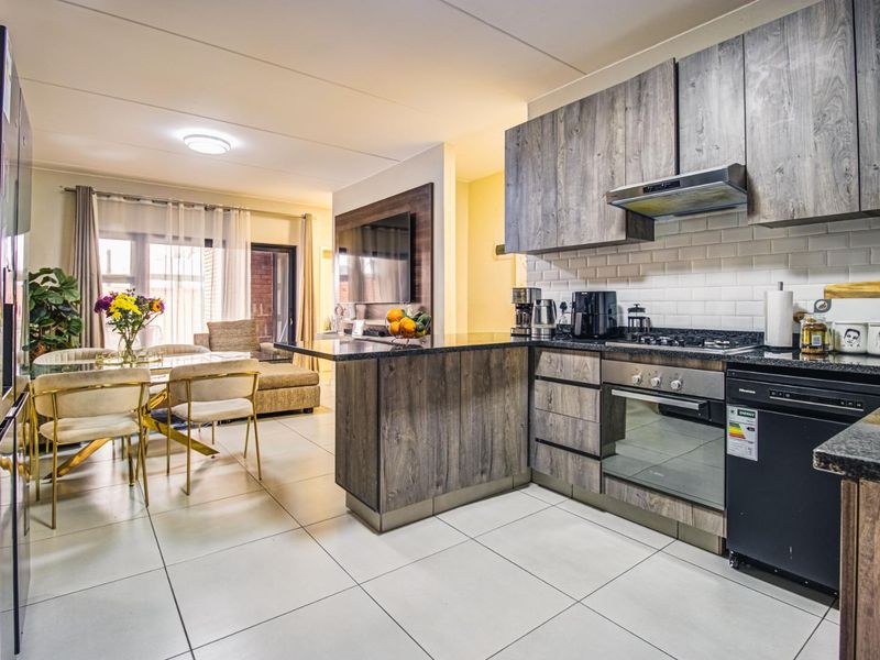 Modern open-plan kitchen and dining area featuring wood-grain cabinetry, granite countertops, and high-quality built-in appliances, flowing into a bright living space.