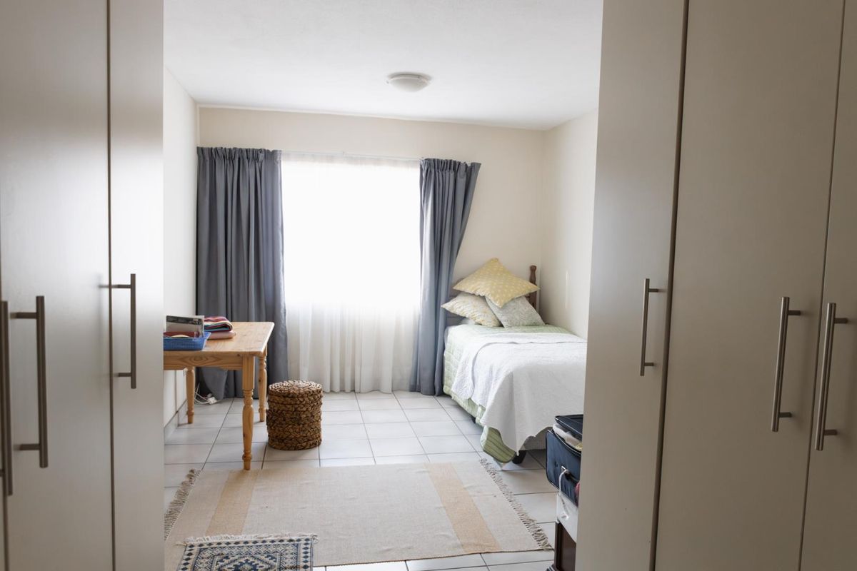 A functional bedroom featuring tiled flooring, built-in cupboards, and a window with curtains, providing a simple and practical living space.