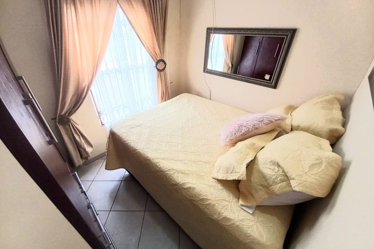 A compact bedroom featuring tiled flooring, built-in wardrobe storage, and a window with security bars.