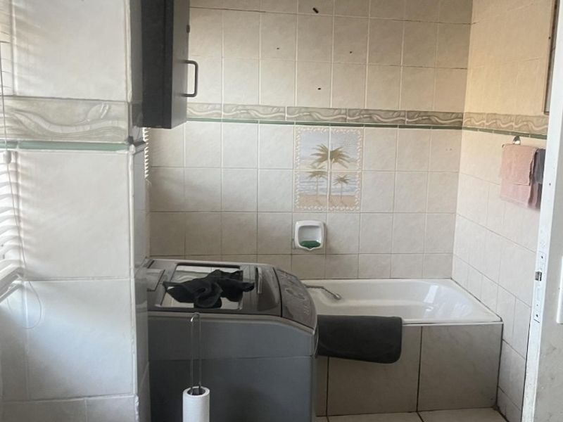 A functional bathroom featuring a built-in bathtub and tiled walls, currently showing signs of wear and requiring cosmetic updates.