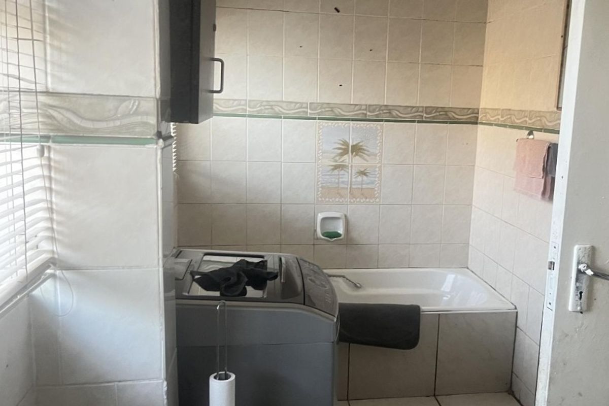 A functional bathroom featuring a built-in bathtub and tiled walls, currently showing signs of wear and requiring cosmetic updates.