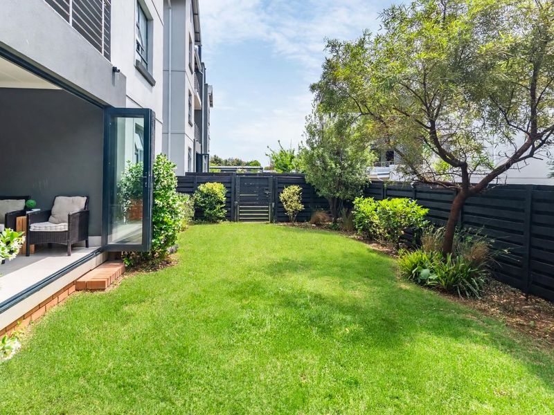 A well-maintained rear garden featuring a manicured lawn, mature trees, and modern timber slat fencing, accessible via large bi-fold doors from the apartment.