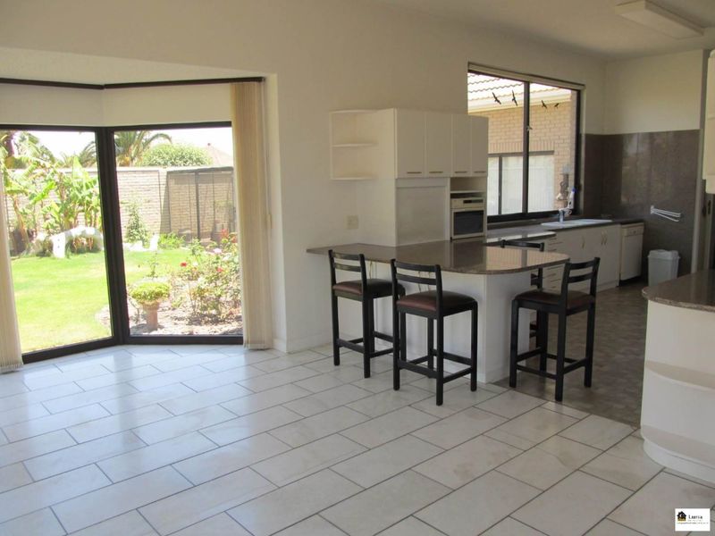 Open-plan kitchen and living area featuring tiled floors, granite countertops, built-in cabinetry, and large sliding glass doors providing direct access to the garden.