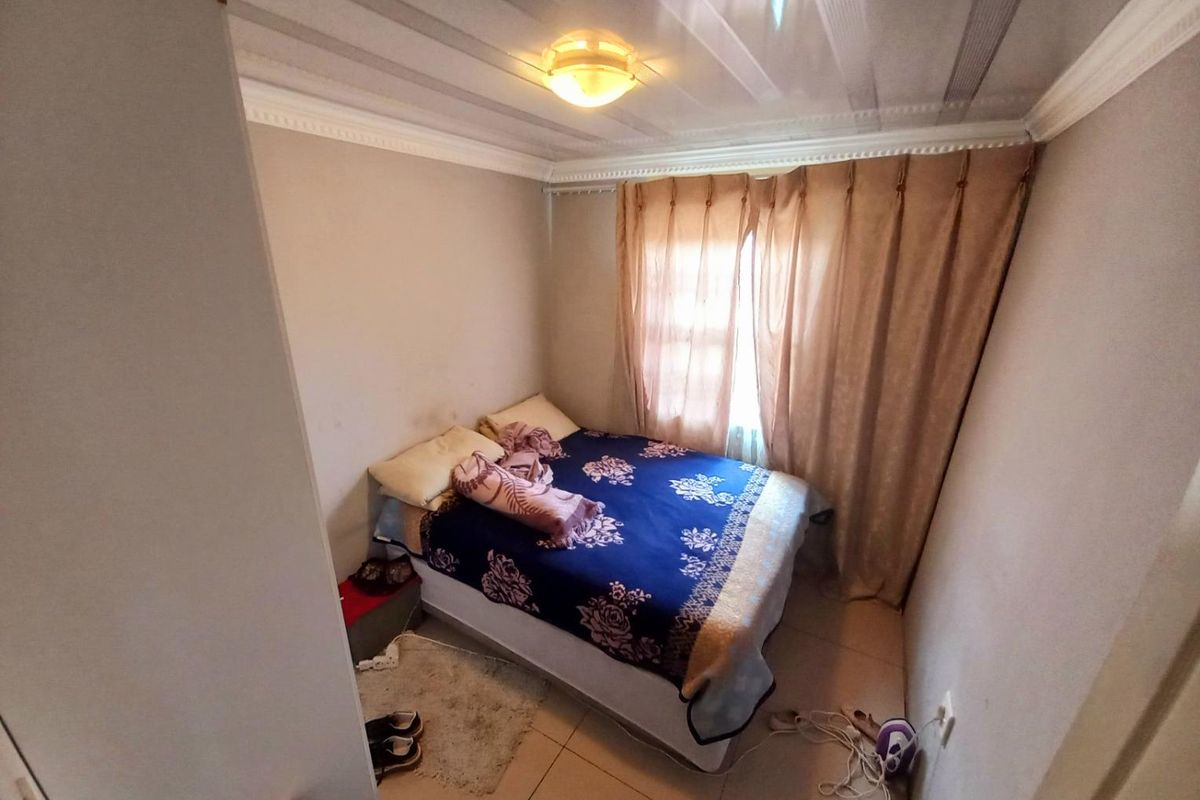 A compact bedroom featuring tiled flooring, crown molding, and a window with curtain treatments.