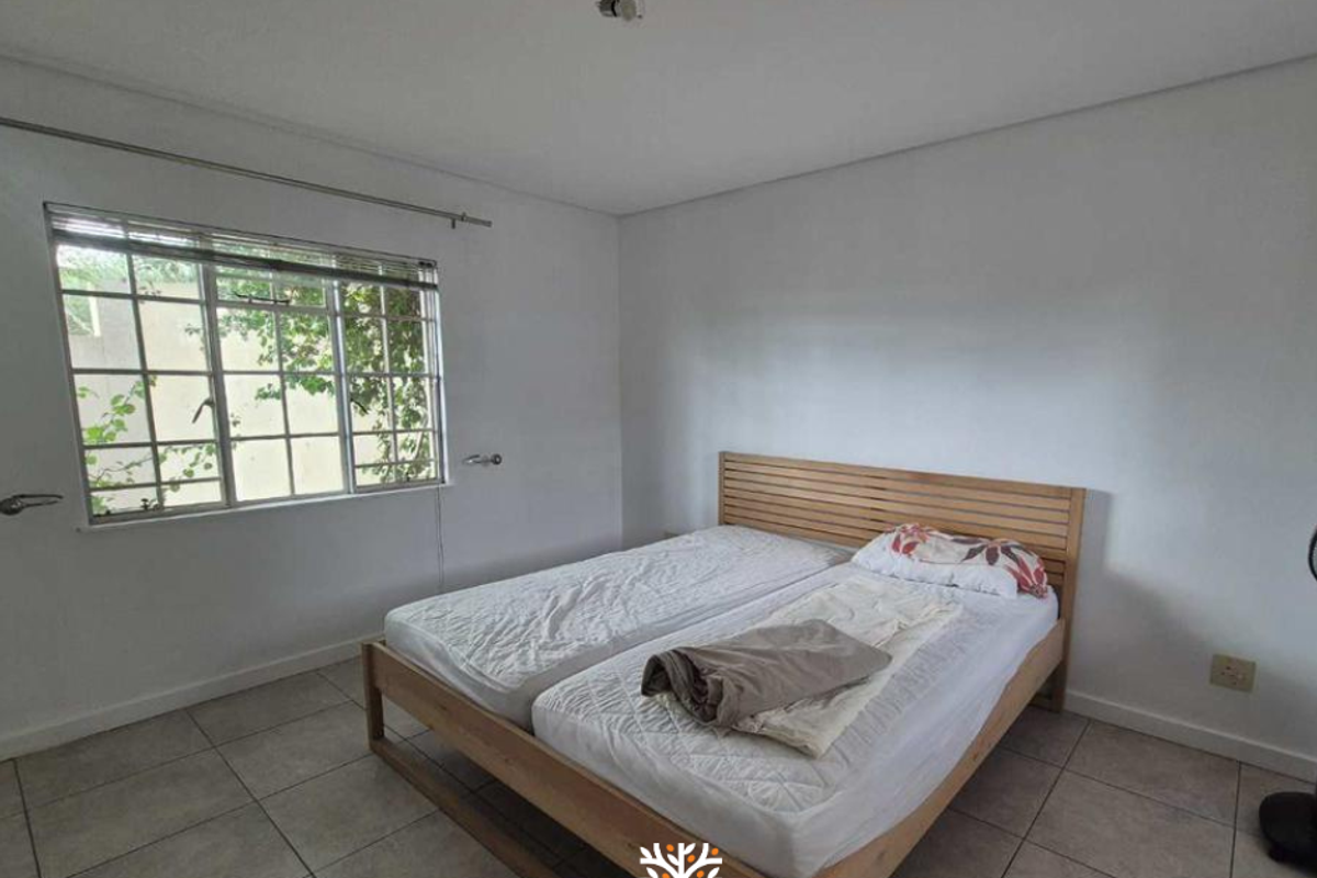 A simple bedroom featuring tiled flooring, a large window with security bars, and a ceiling-mounted light fixture.