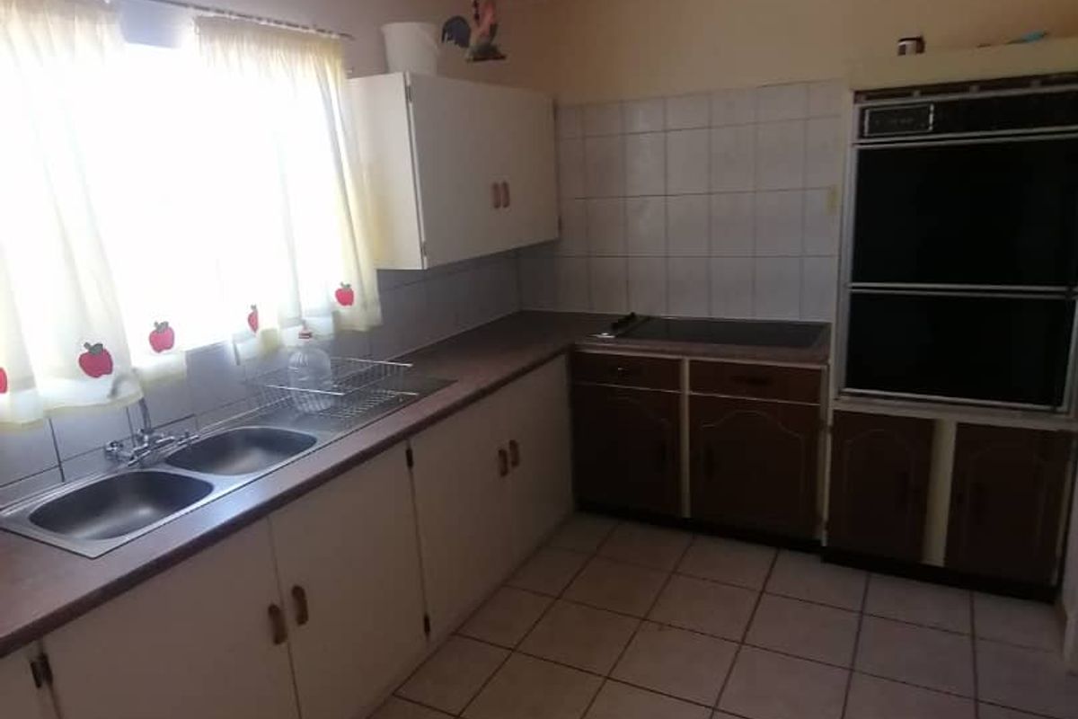 A dated kitchen featuring original cabinetry, tiled flooring, a built-in wall oven, and a double-basin sink with a window view.