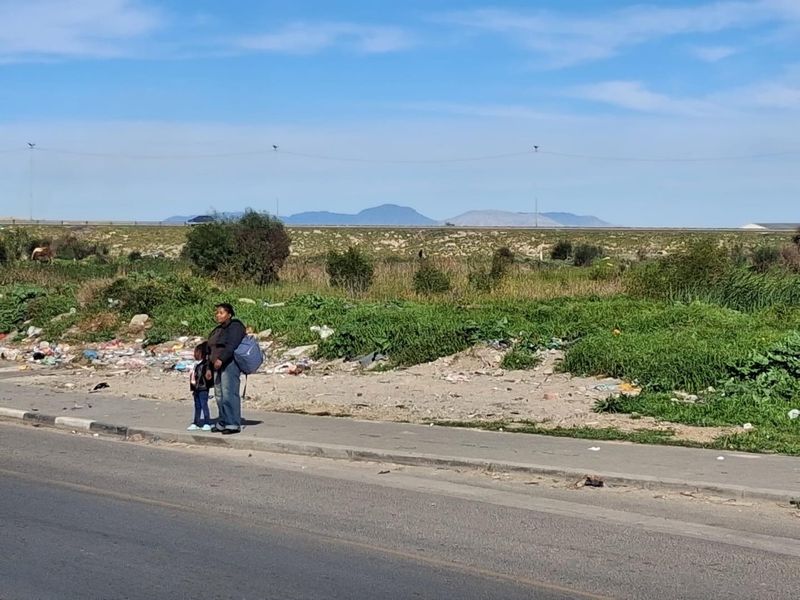 Street-level view of the property frontage showing a paved sidewalk adjacent to an undeveloped agricultural plot with distant mountain views.