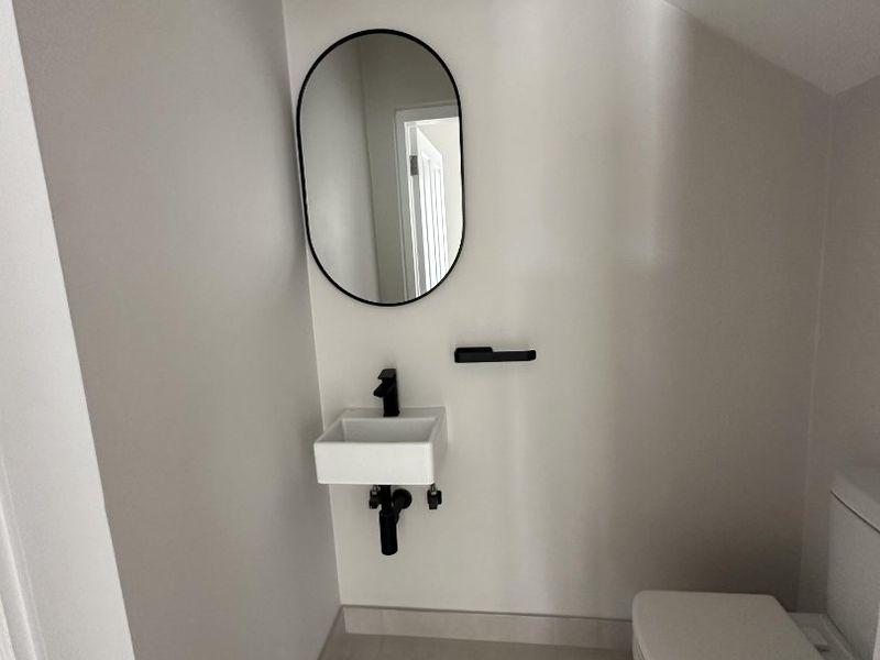 A modern, compact powder room featuring a wall-mounted basin, black fixtures, and a clean, minimalist aesthetic.